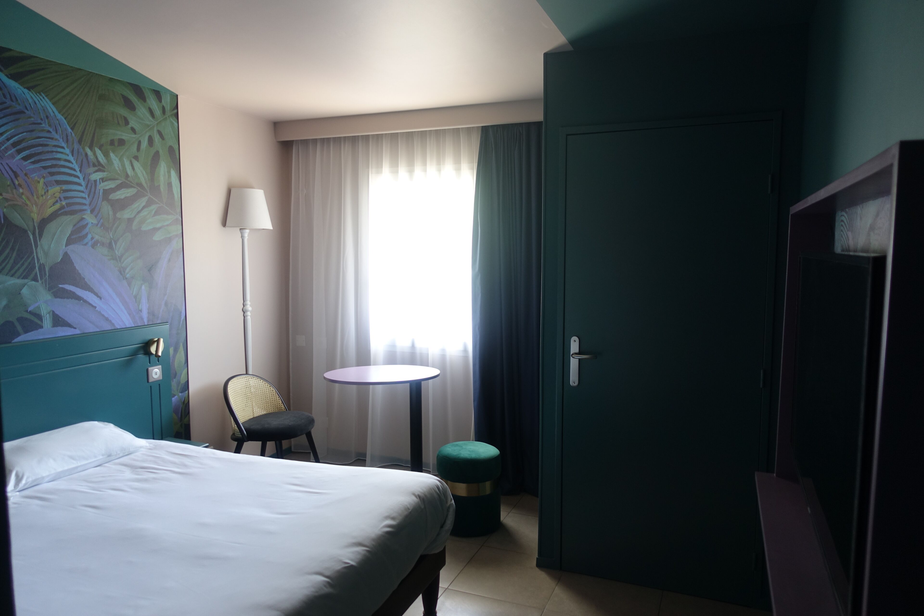 Habitación de hotel con cama, una silla, una mesita redonda, una lámpara y una puerta.
