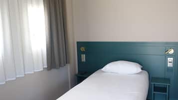 A single bed with a white pillow, a teal headboard, a bedside table with a remote control, and a power outlet on the wall.