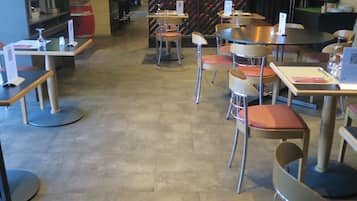 Een modern restaurant met diverse zitmogelijkheden, waaronder ronde tafels en stoelen, een bar met een toog en een decoratieve wand met een geometrisch patroon.