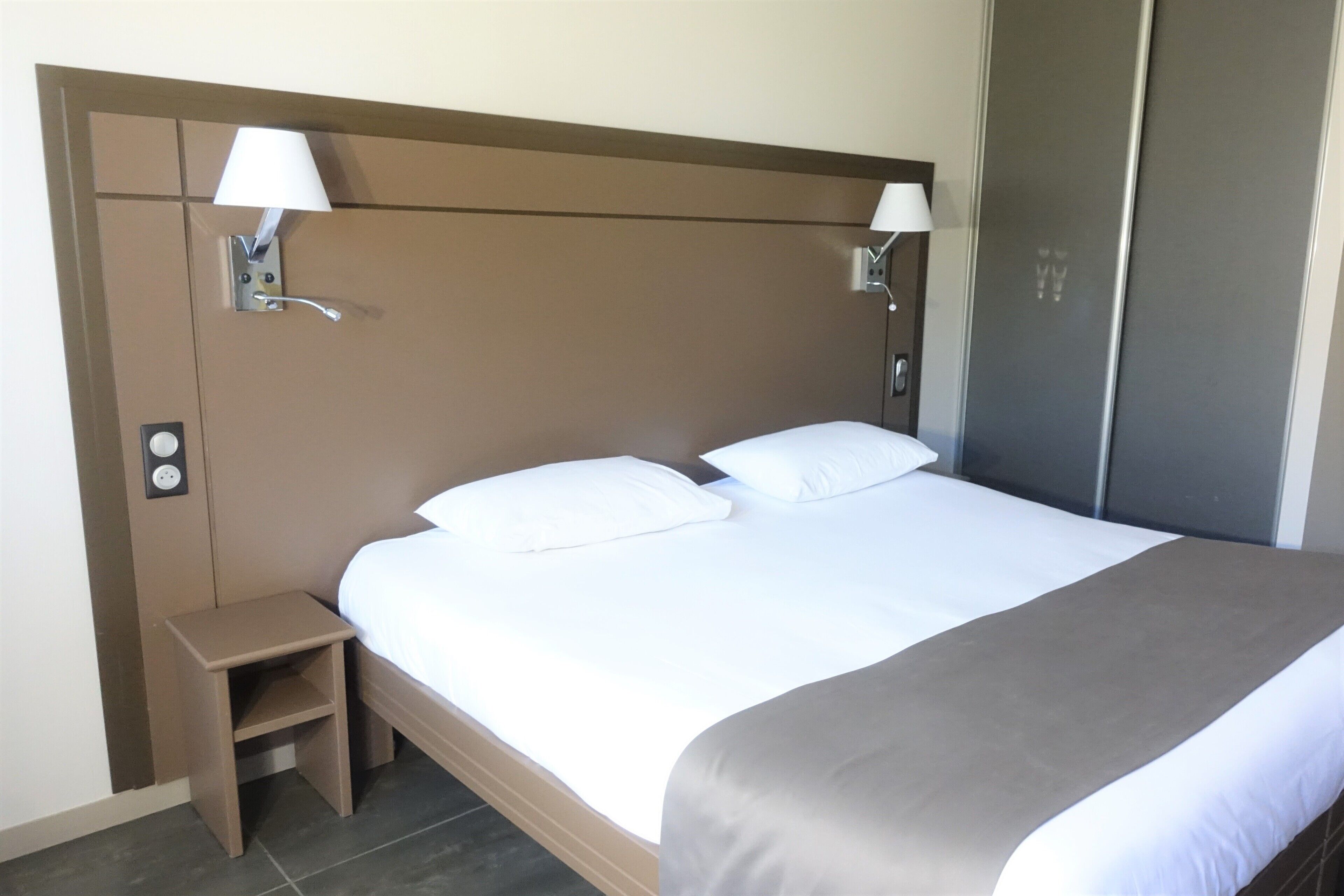 Ein Hotelzimmer mit einem großen Bett, zwei Nachttischlampen, einem Nachttisch und einem Kleiderschrank.