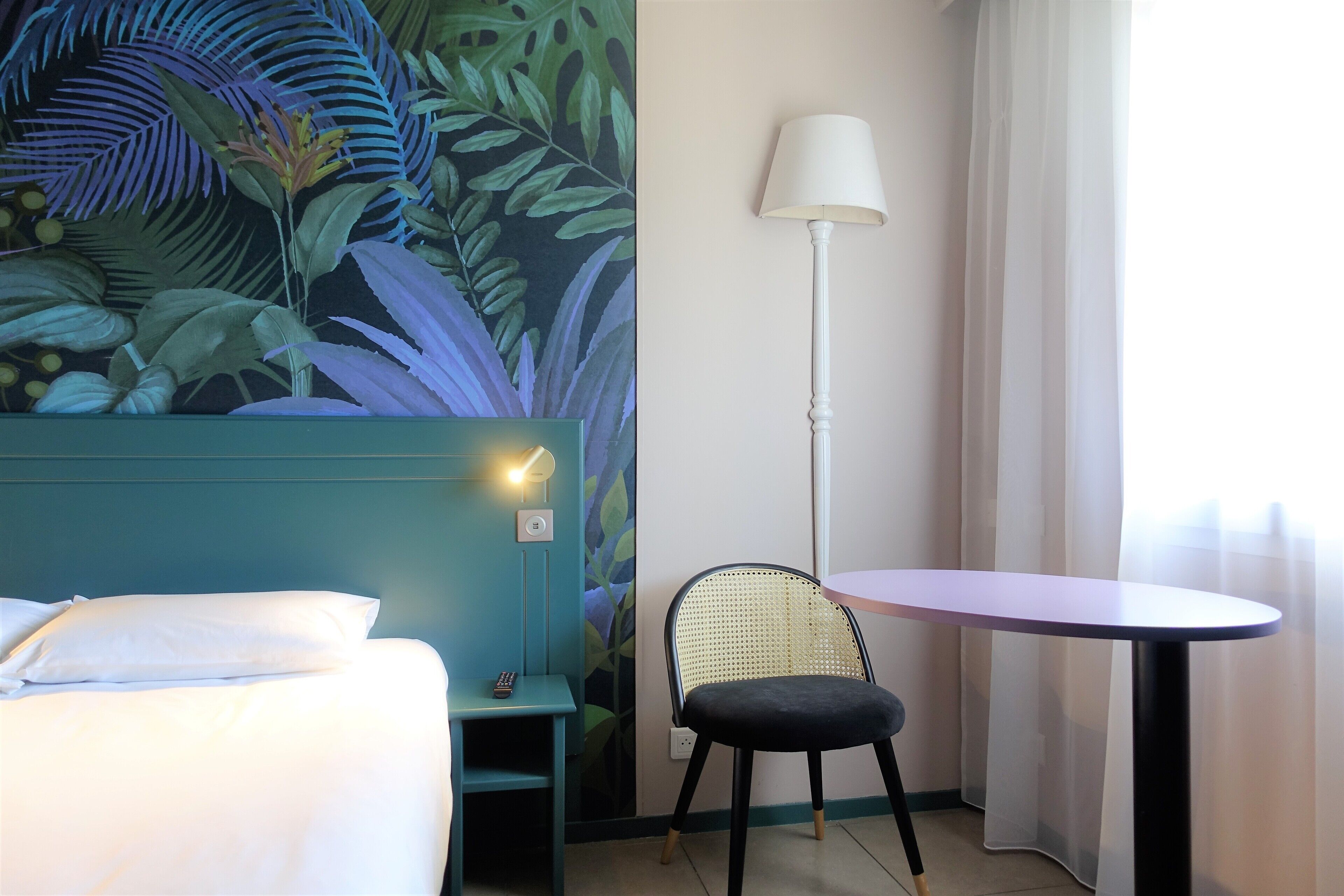 A hotel room with a bed, a desk, a chair, a small table, and a wall mural.