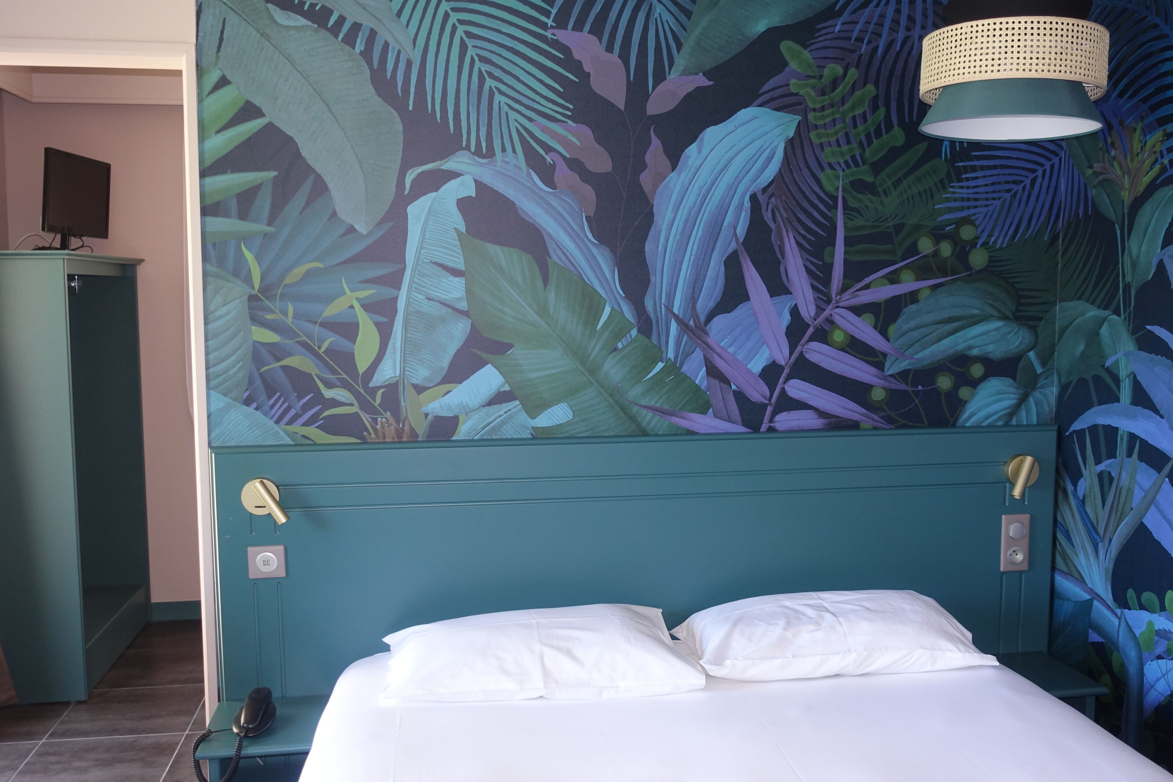 A room with a bed, a telephone, and a wall with a tropical leaf mural.