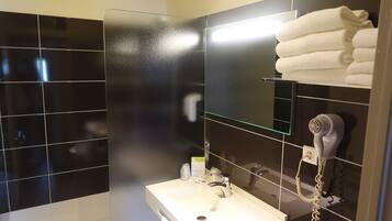 Un baño con lavamanos blanco, cabina de ducha de vidrio y secador de pelo montado en la pared.