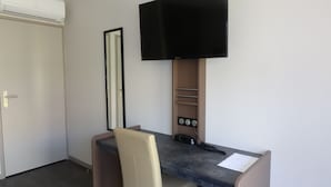 A small office space with a desk, chair, and a mounted flat-screen TV. - Hôtel Grand Confort Le Moulin Rouge (Terrasson-la-Villedieu)