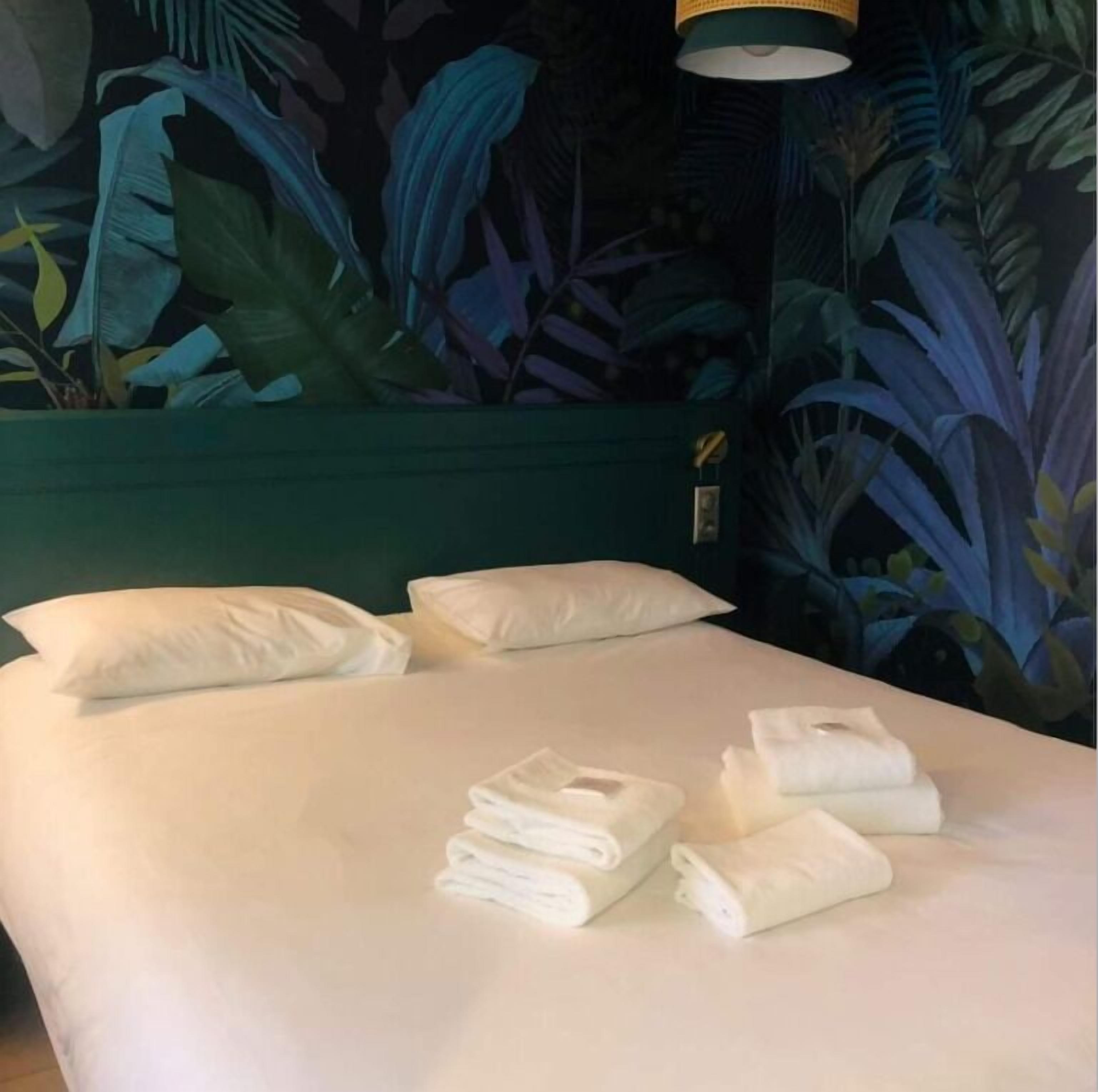 A neatly made bed with white linens and pillows, a green headboard, and a tropical mural on the wall.