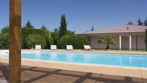 A swimming pool with lounge chairs, a covered building, and surrounding greenery. - Hôtel Grand Confort Le Moulin Rouge (Terrasson-la-Villedieu)