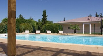 A swimming pool with lounge chairs, a covered building, and surrounding greenery.