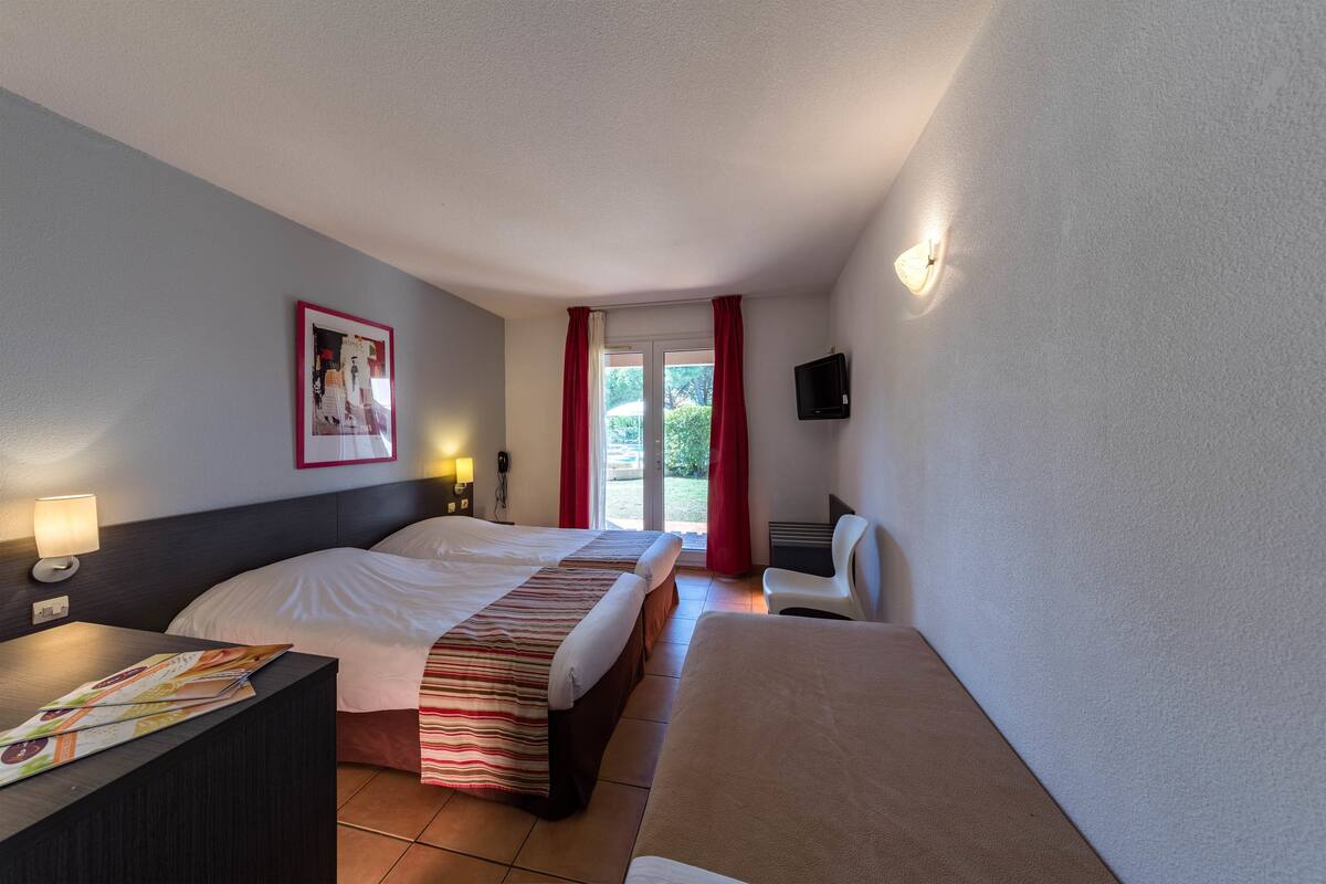 A hotel room with two beds, a desk, a chair, a TV, and a window with curtains.