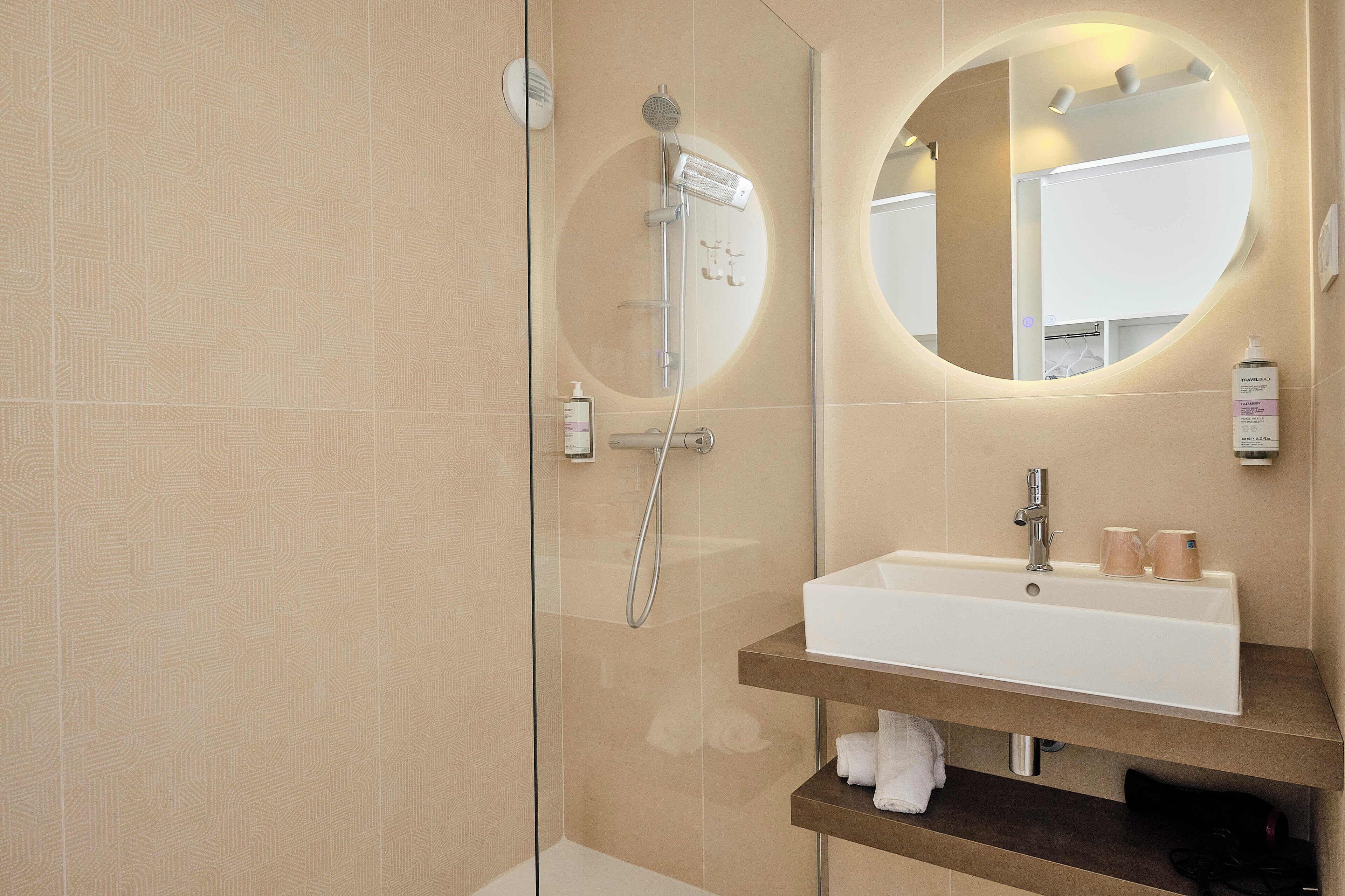 Un bagno moderno con cabina doccia in vetro, un lavabo bianco con ripiano in legno e uno specchio rotondo.
