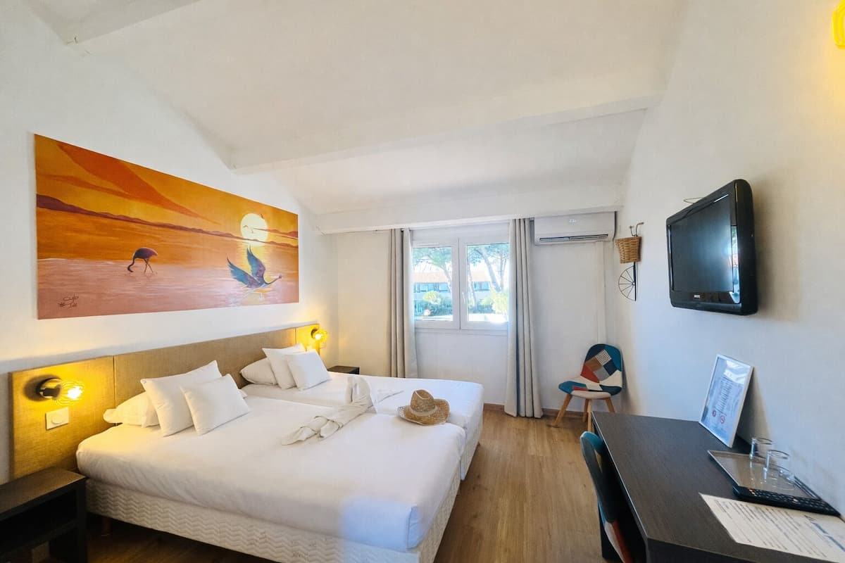 A hotel room with a bed, bedside tables, a desk, a chair, a TV, and a painting on the wall.