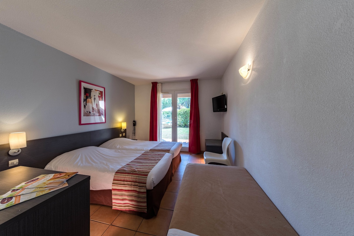 Una habitación de hotel con dos camas, un escritorio, una silla, un televisor y una ventana con cortinas.