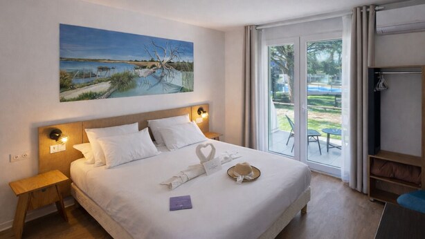 Habitación de hotel con una cama grande, un cuadro en la pared y vistas a una piscina y jardín a través de la puerta de vidrio.