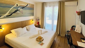 Habitación de hotel con una cama grande, un escritorio con silla, un televisor y un cuadro de pájaros en la pared.