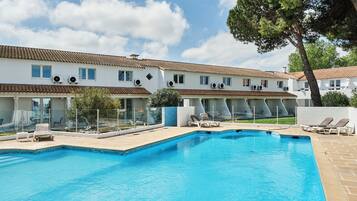 Una piscina con lettini, cielo sereno e un edificio con diverse finestre e condizionatori.