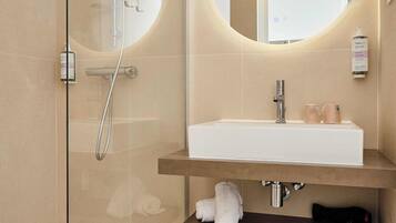 Un baño moderno con ducha de vidrio, un lavamanos blanco con espejo y un perchero para toallas.