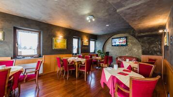 A restaurant with wooden floors, red chairs, and tables set with white tablecloths.