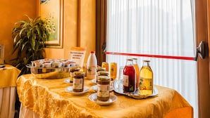 A table with food items and condiments, a potted plant, and a painting on the wall. - Hotel Au Soleil (Saint-Vincent)