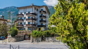 A multi-story hotel with balconies, a stone wall, and a mountain backdrop. - Hotel Au Soleil (Saint-Vincent)