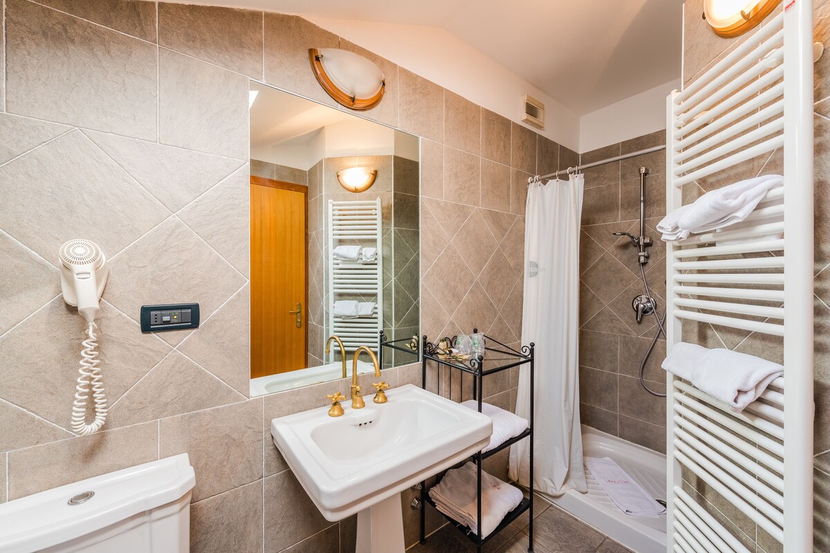 Un baño moderno con un lavamanos blanco, un espejo, un perchero para toallas y una zona de ducha.