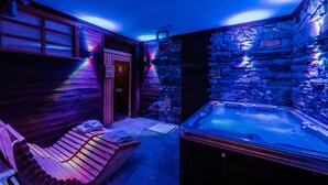 A spa area with a hot tub, wooden benches, and stone walls. - Hotel Au Soleil (Saint-Vincent)