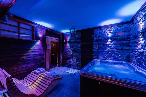 Un área de spa con un jacuzzi, bancos de madera y paredes de piedra.