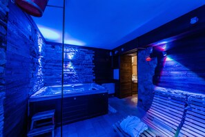 Un moderno cuarto de spa con pared de piedra, una bañera de hidromasaje y bancos de madera.