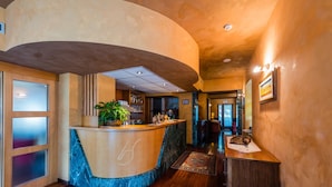 A reception area with a curved counter, wooden flooring, and a potted plant. - Hotel Au Soleil (Saint-Vincent)