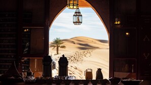 A desert view through an arched doorway with a table set for breakfast, including a coffee pot, teapot, and various dishes. - Hotel Kanz Erremal (Taouz)