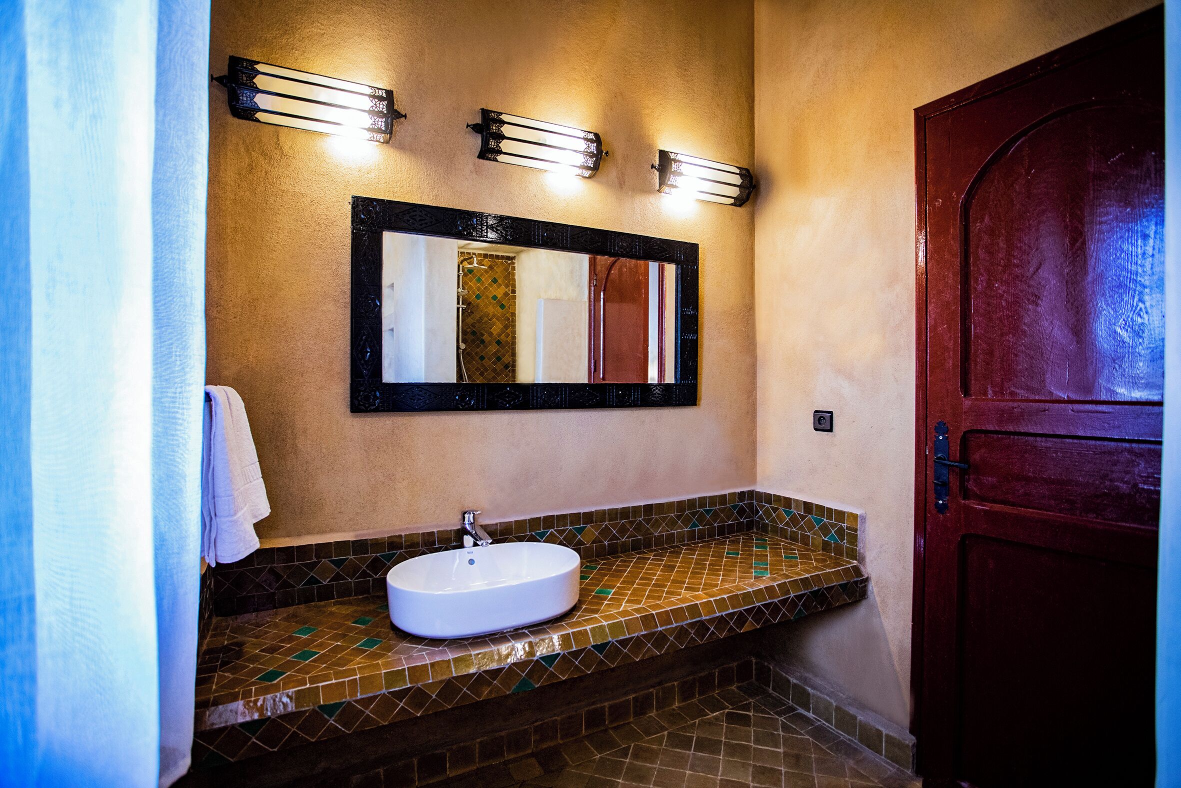Un bagno con lavandino bianco, uno specchio e uno schienale piastrellato.