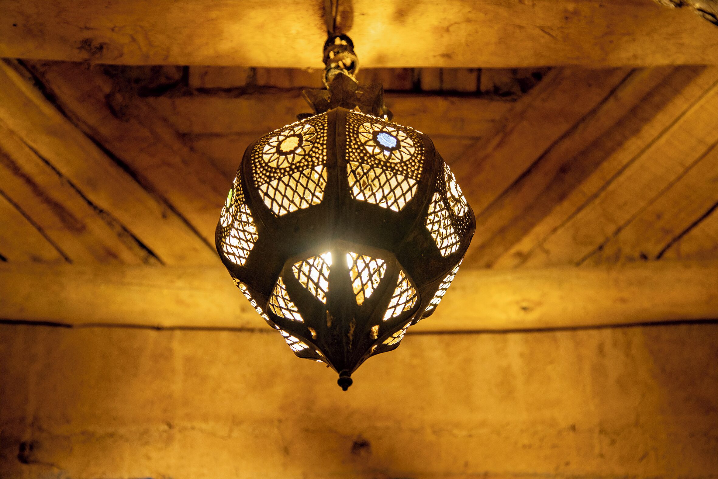 A hanging lantern with intricate lattice design, suspended from a wooden ceiling.