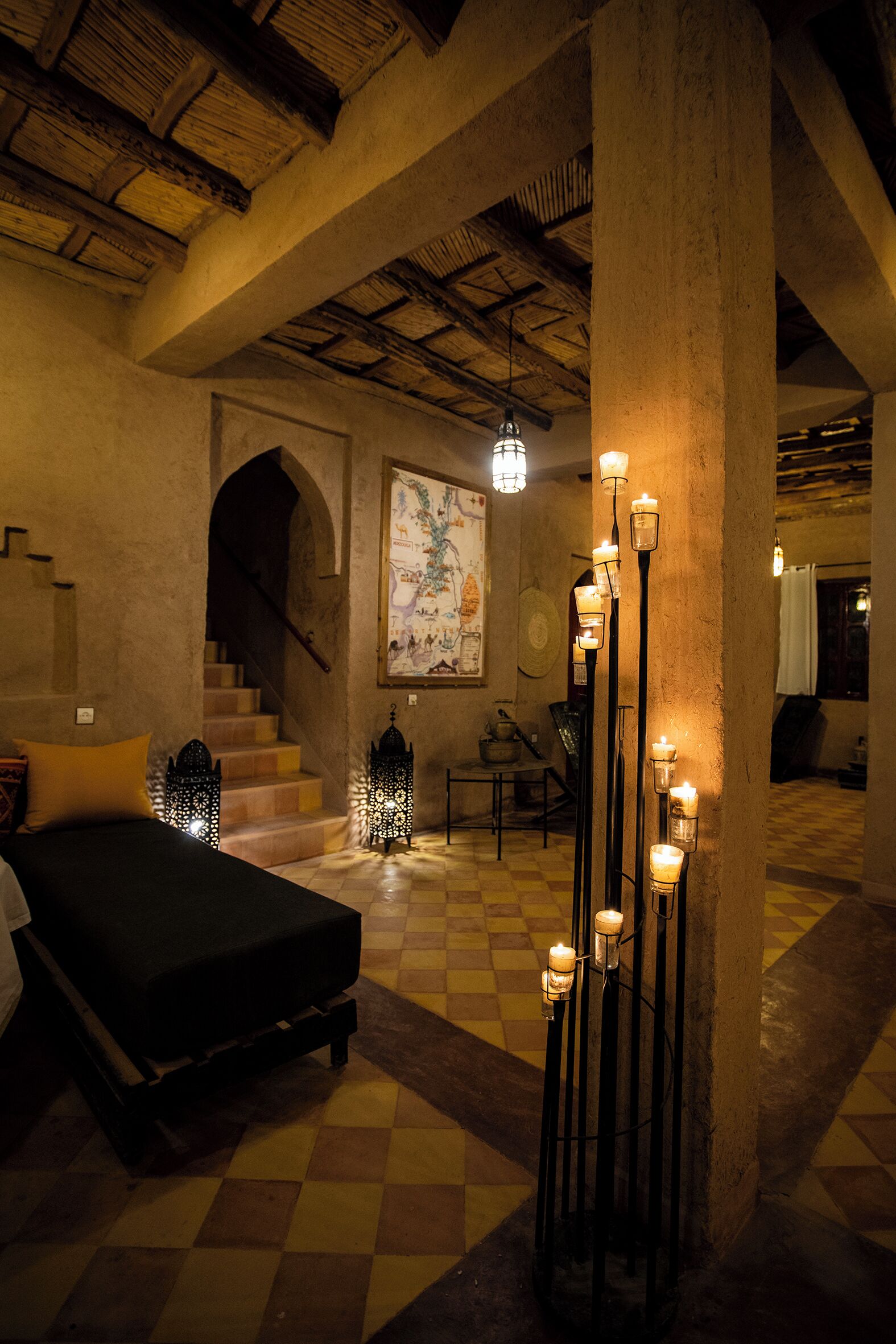 A room with a checkered floor, a bed, a staircase, and wall-mounted lanterns.
