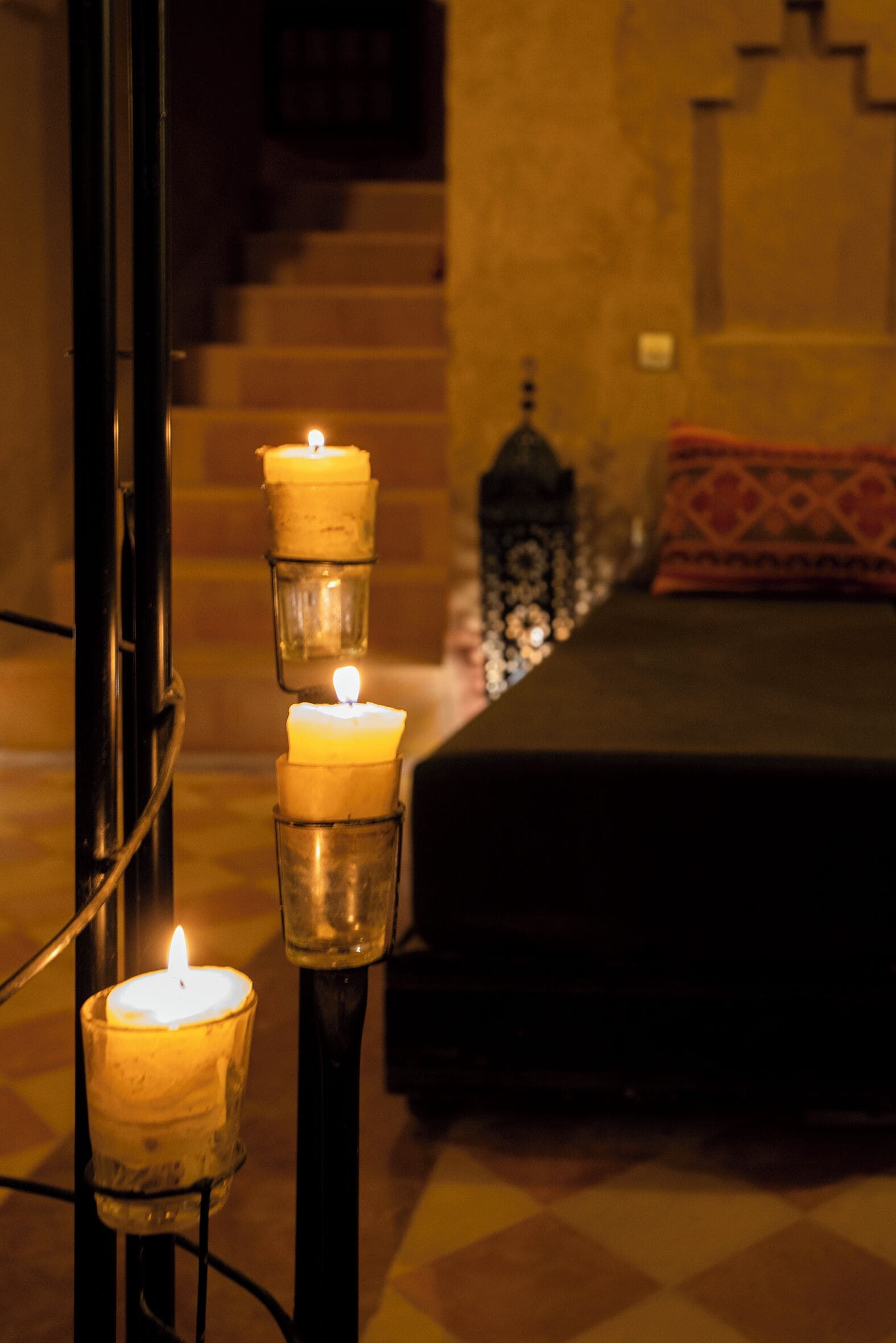 A room with a bed, a staircase, and three lit candles on a stand.