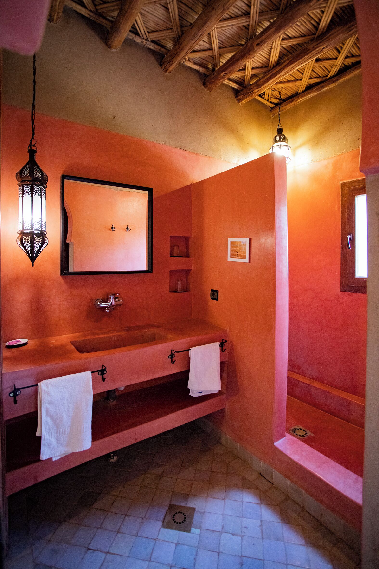 Un baño con techo de madera, un espejo grande, un lavamanos con dos toallas e iluminación colgante.