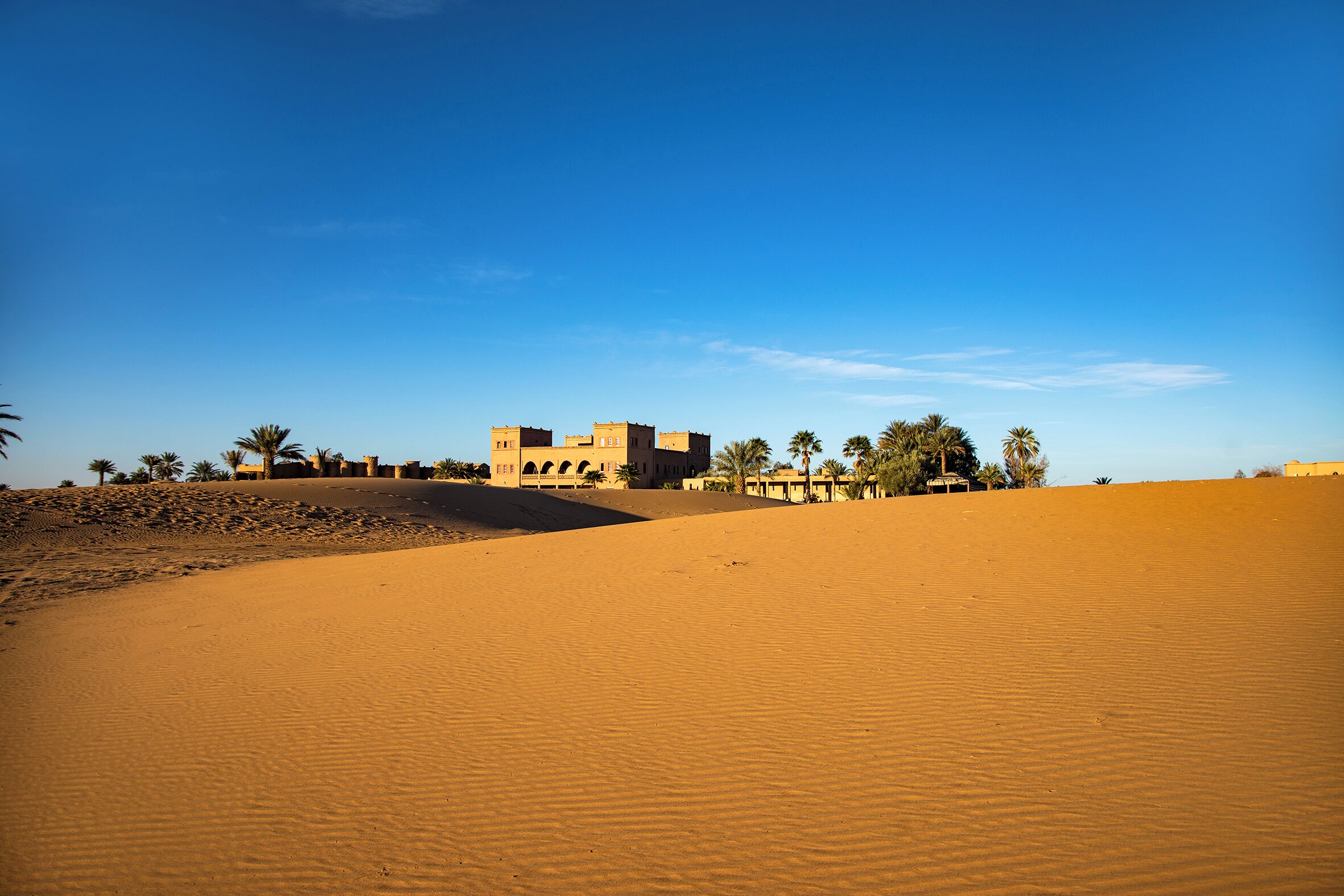 A desert landscape with sand dunes and a building with arches.
