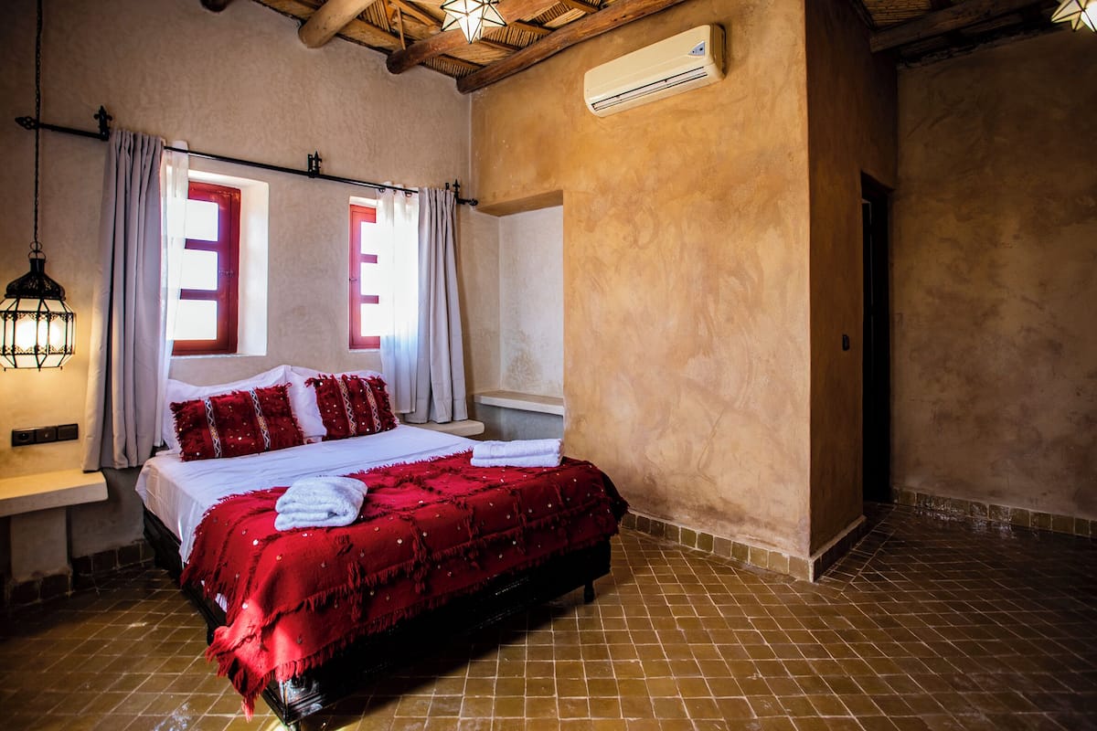 Un dormitorio con cama, mesita de noche, aire acondicionado y ventana con cortinas.