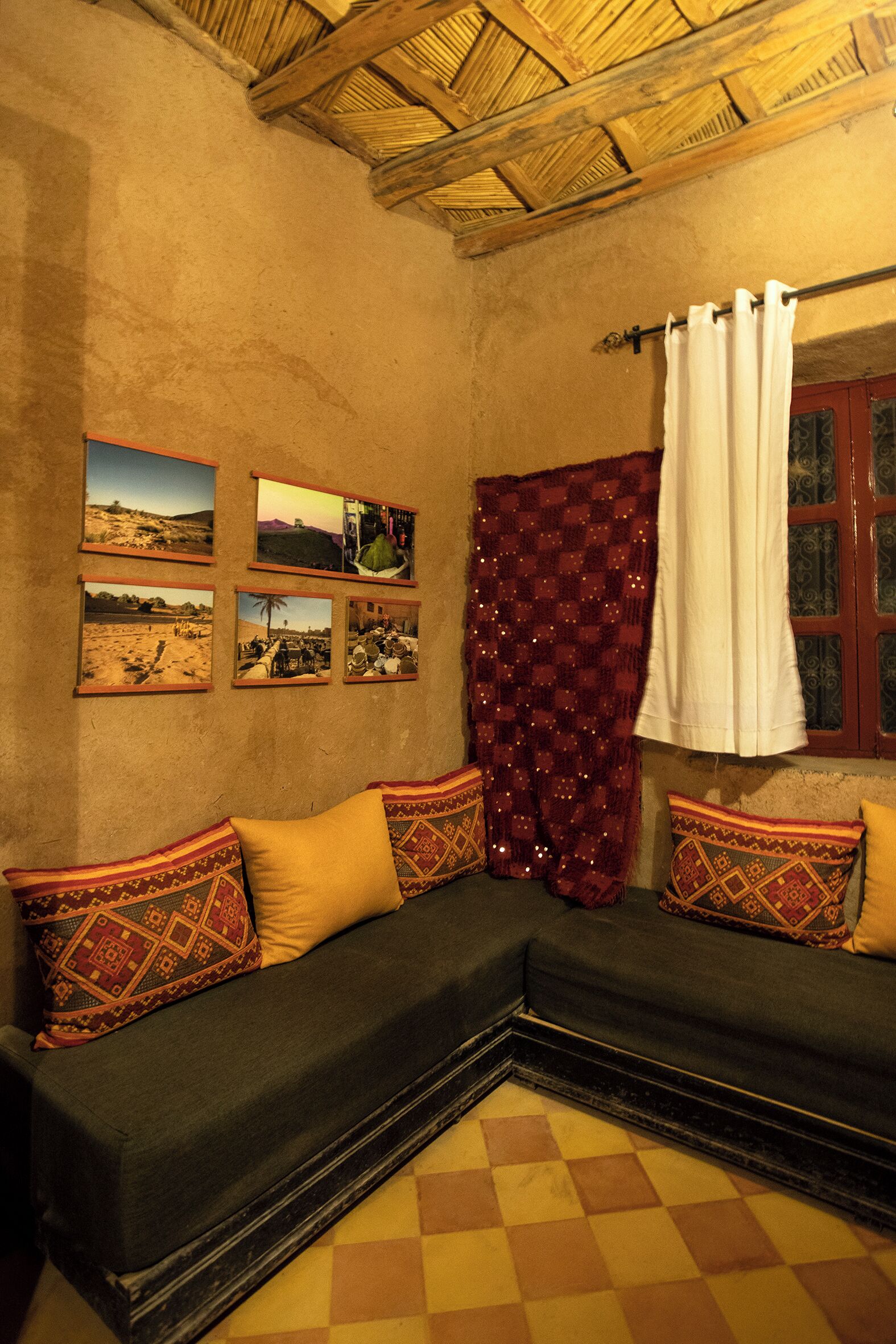 Una habitación con piso a cuadros, un sofá oscuro con cojines estampados, una cortina roja y cuadros en la pared.
