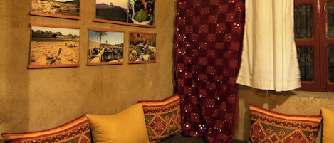 Una habitación con piso a cuadros, un sofá oscuro con cojines estampados, una cortina roja y cuadros en la pared.