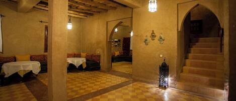A dining area with checkered flooring, tables with white tablecloths, and a staircase leading to an upper level.