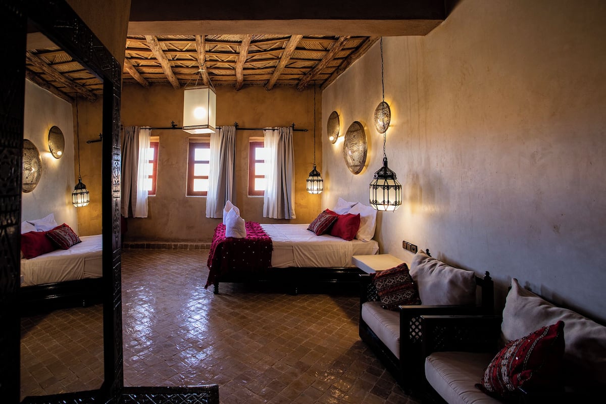 Una habitación tradicional con techo de madera, dos camas con ropa de cama roja y blanca, un sofá y faroles colgantes.
