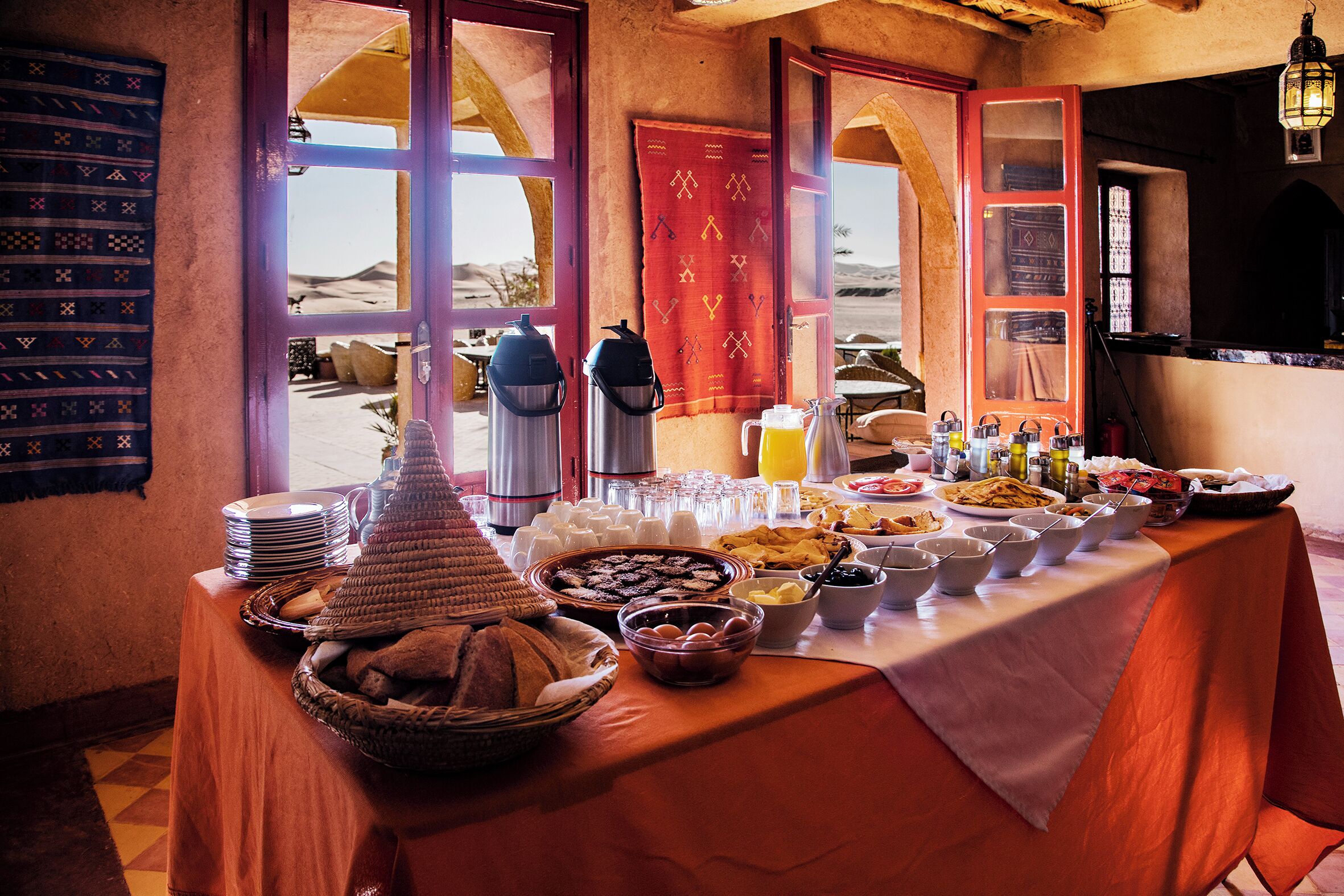 Een buffettafel met diverse gerechten en dranken, met in de achtergrond een woestijnlandschap en traditionele decoratie.