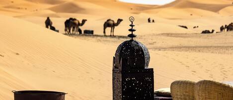 A desert scene with sand dunes, a traditional lantern, a metal pot, and a woven chair.