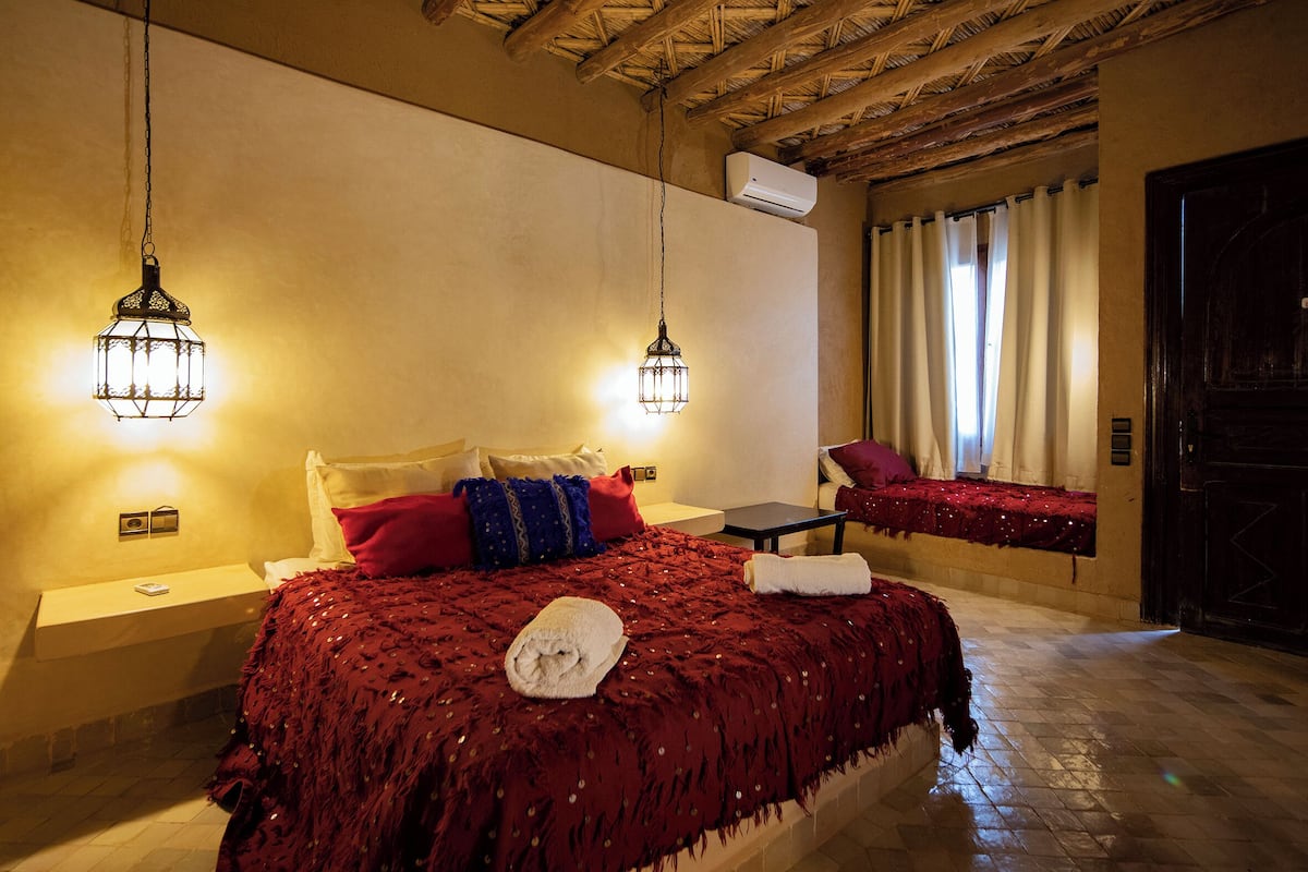 Un dormitorio con una cama grande, dos mesitas de noche, una mesita auxiliar, una silla y una toalla sobre la cama y un edredón.