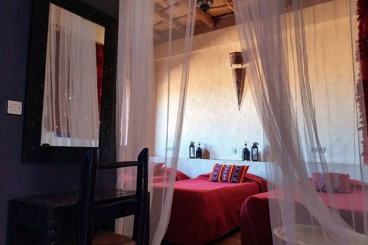 Una habitación con una cama, una silla, una mesa y un espejo.