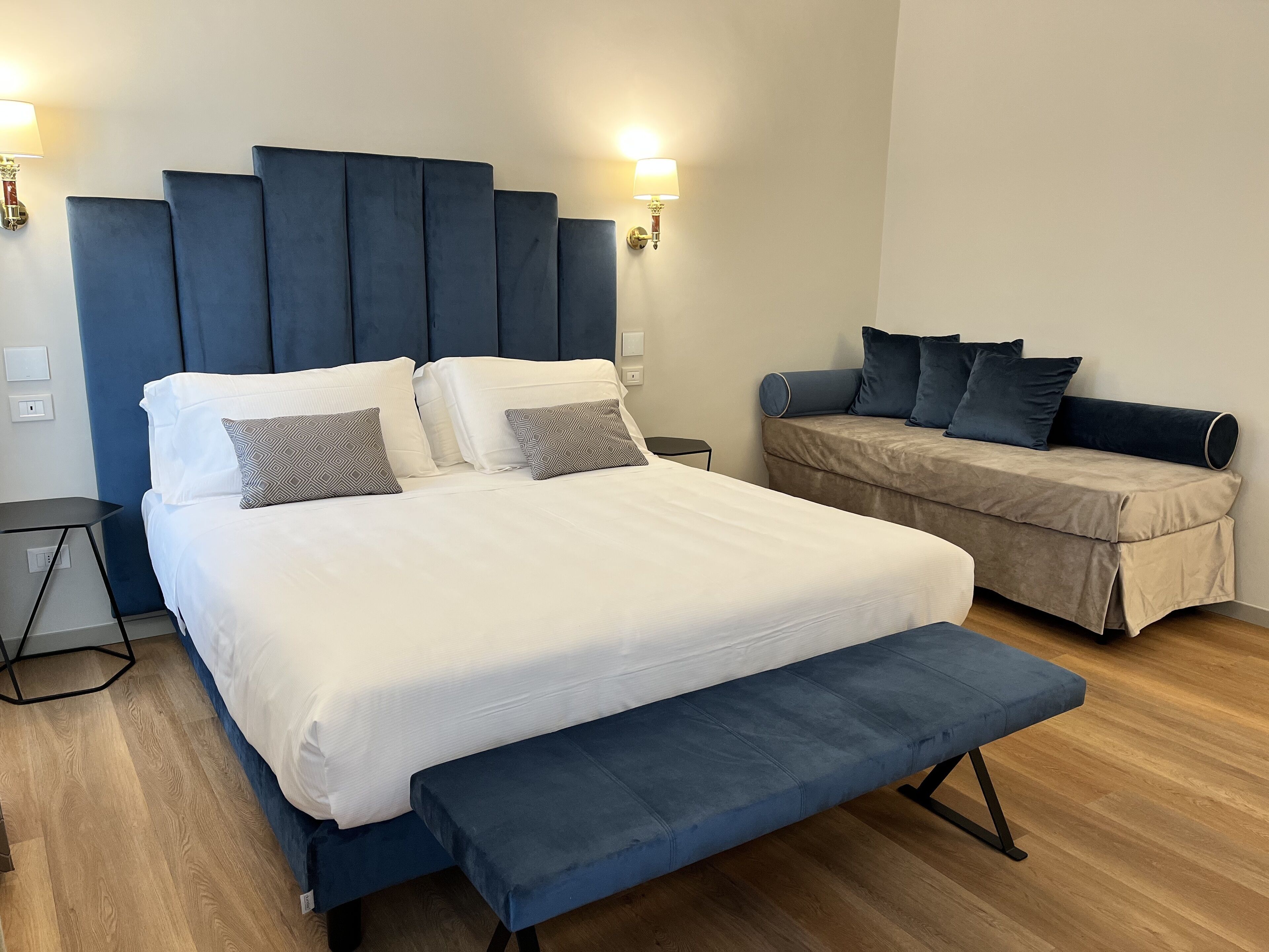 A modern bedroom with a large bed, a bench, a sofa, and two bedside tables.
