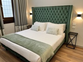 Un letto rifatto con cura, una testiera imbottita verde, biancheria bianca e due comodini con lampade a parete.