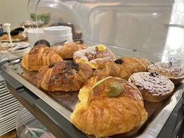 Una selezione di pasticceria esposta in una vetrina, tra cui croissant e muffin con decorazioni come gocce di cioccolato e zucchero a velo.