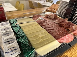 Mostrador de charcutería con diversos tipos de carne y queso, incluyendo salami en rodajas, prosciutto y queso Philadelphia.