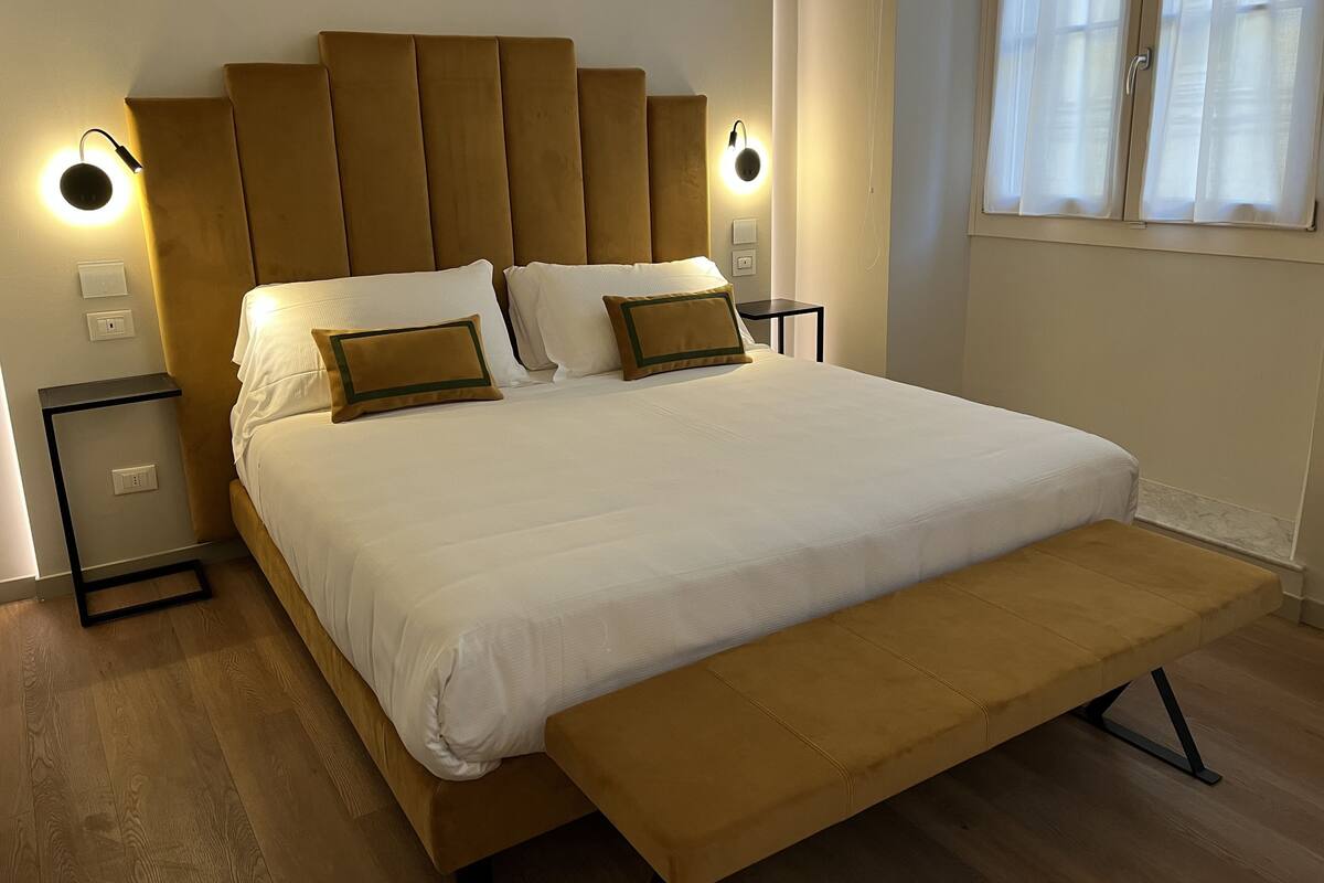 Een moderne slaapkamer met een groot bed, twee nachtkastjes en een bankje.