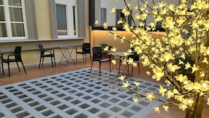 Zona d'estar a l'aire lliure amb un paviment estampat, cadires i un arbre amb flors il·luminades.