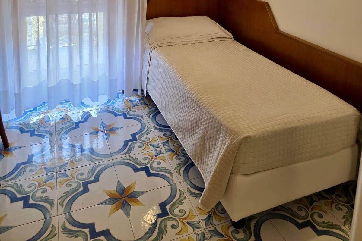 Une petite chambre avec un lit simple, une tête de lit en bois, un mur d’accent vert et un sol à motifs.
